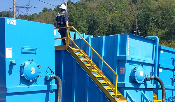Worker inspecting E-Tank 21000-gallon frac tanks using safety staircase, demonstrating proper tank operation and inspection procedures