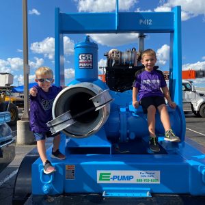 Children sitting on E-Pump industrial pump display at Touch-a-Truck event, learning about high-flow pump equipment and E-Tank environmental services