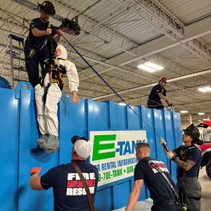 Firefighters performing confined space rescue training, lifting mannequin from E-Tank rental tank during safety exercise