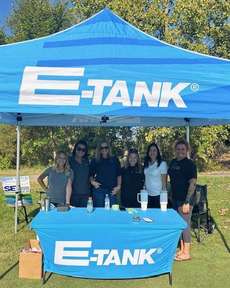 E-Tank team members at branded tent during E-Tank Classic charity golf tournament supporting The Legacy Project, showcasing community involvement and sponsorship presence on the course